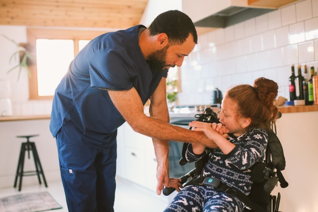 A support worker helping a smiling woman in a wheelchair at home